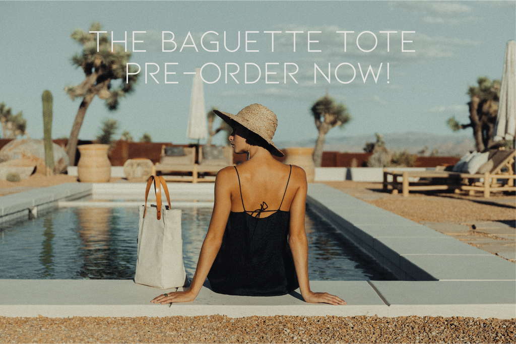 A woman sits on the edge of a pool wearing a sun hat with a leather-handled canvas tote