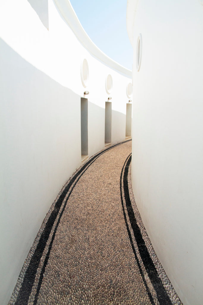 A pebble path with clean whtte walls on bother sides illuminated by the sun