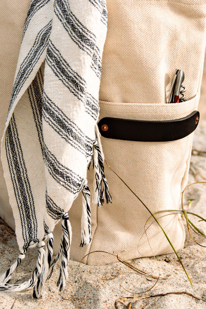 A leather-handled canvas tote with a beach towel and corkscrew 