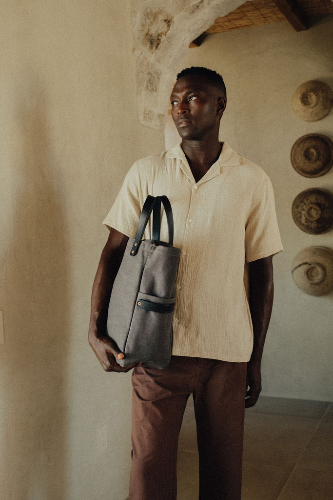 A man standing with a leather-handled canvas tote in his hand