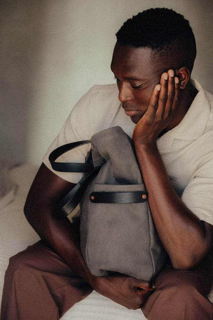 A man sits with his head in one hand and a leather-handled canvas tote in the other