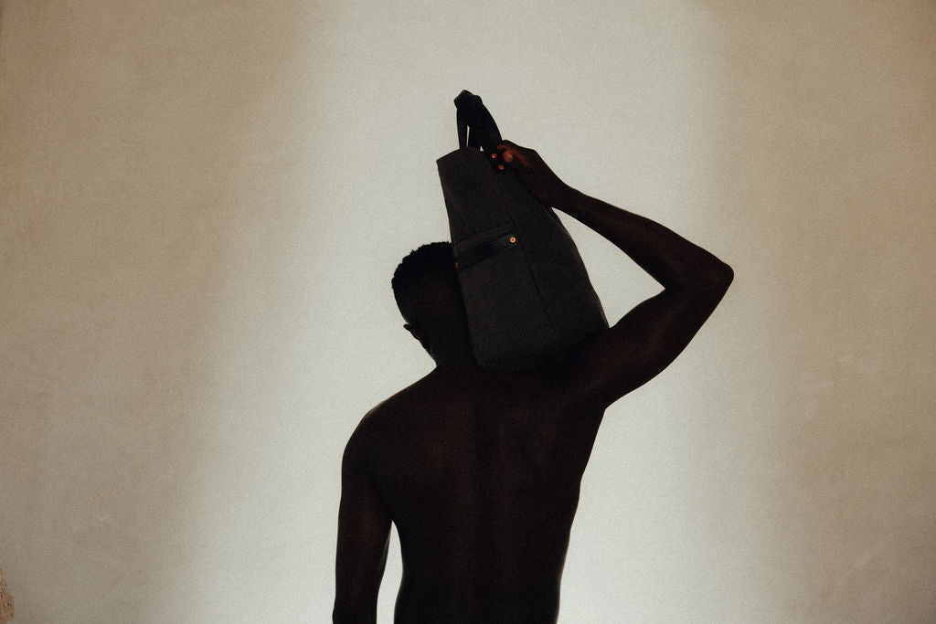 Silhouette, a man stands with a leather-handled canvas tote on his shoulder