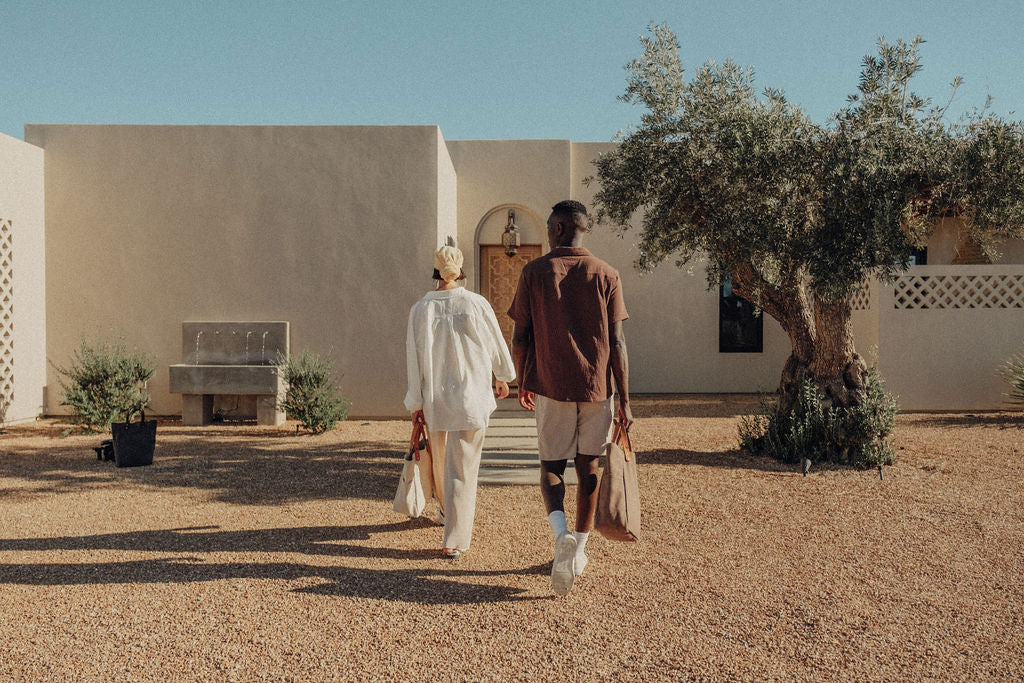 A man and woman walk towards their front door both holding a leather-handled canvas tote