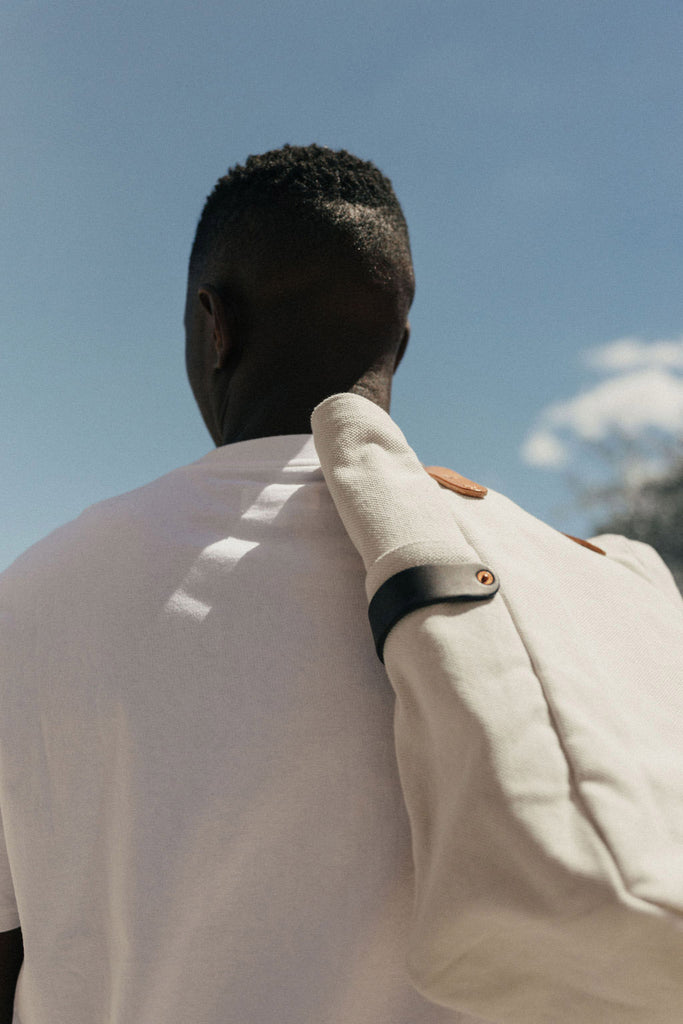 A man stands against a blue sky with a leather-handled canvas tote slung over his shoulder