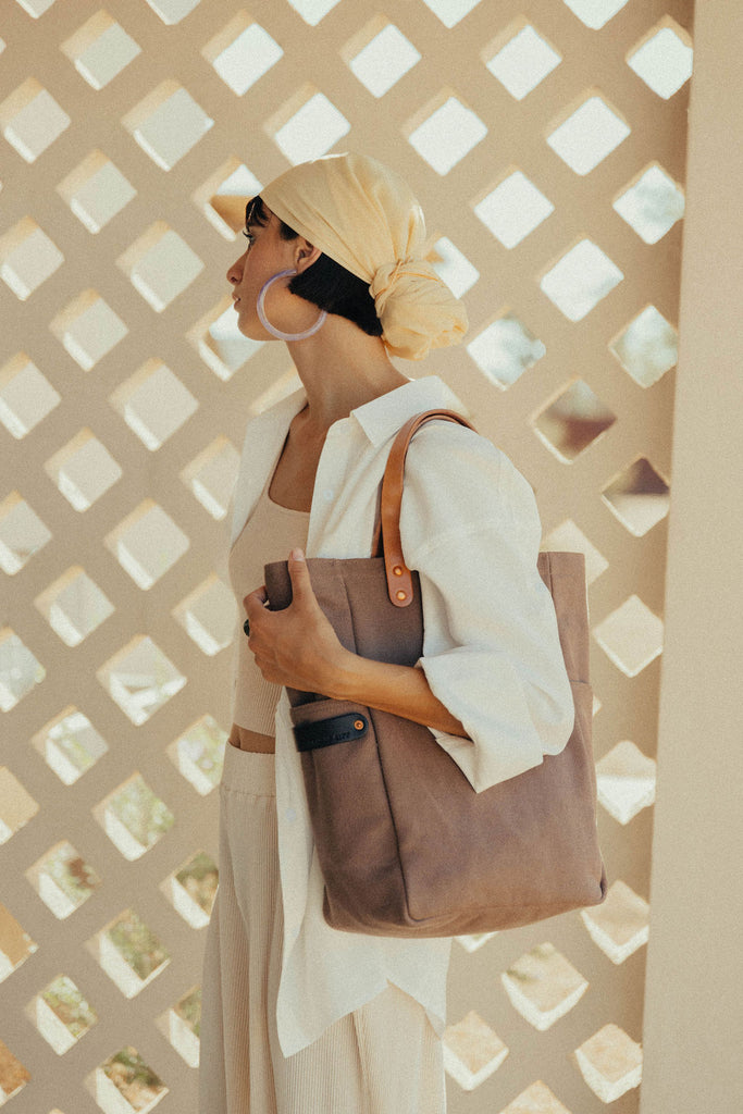 A woman stands with a leather-handled canvas tote on her shoulder