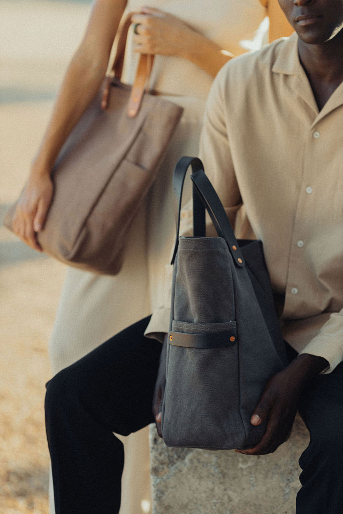 Man sitting and woman standing holding The Baguette Tote made of duck canvas and veg-tanned leather