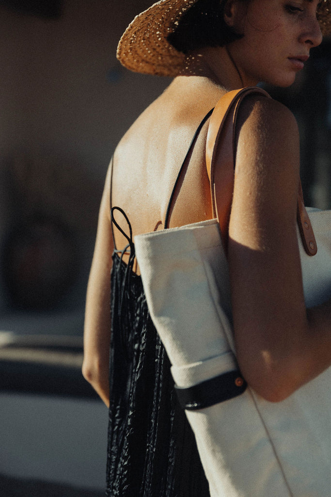 A woman standing with a leather-handled canvas tote hanging from her shoulder